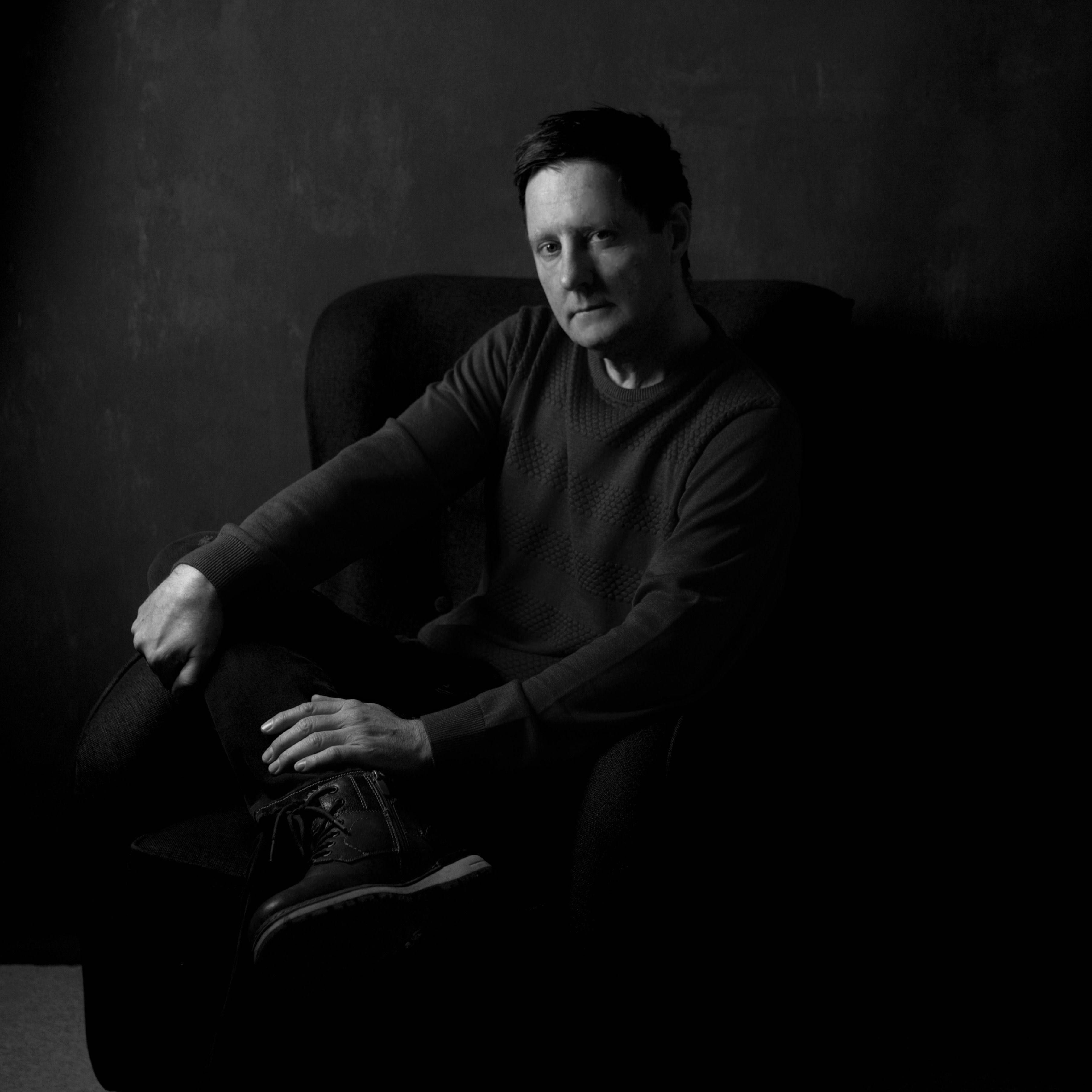 Artistic black and white portrait of a man sitting in a chair, conveying a moody tone.