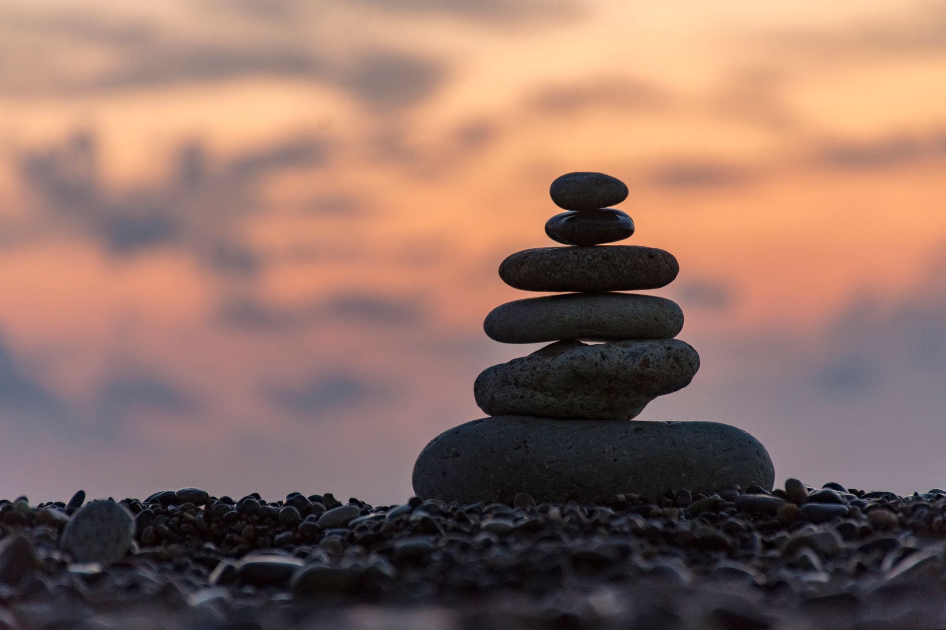 Tranquil image of balanced stones on a beach at sunset, suggesting harmony and meditation.