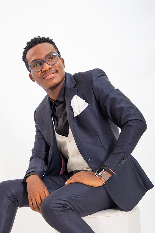 Free Smiling African man in a stylish blue suit, white shirt, and eyewear sitting on a white background. Stock Photo