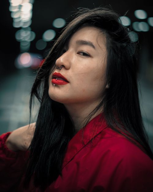Free Close-up of a woman with lip and septum piercings, wearing red lipstick and a red shirt, confidently posing. Stock Photo