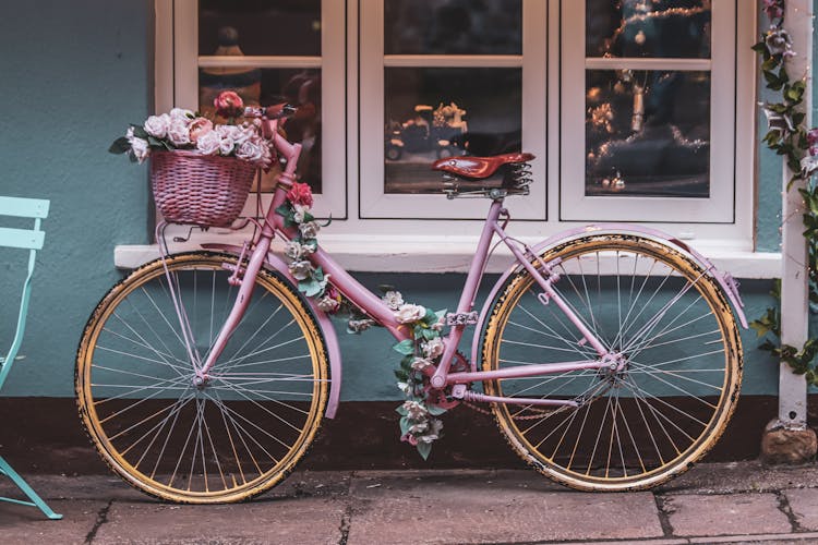 A Vintage Bicycle Decorated With Flowers Parked By A Window