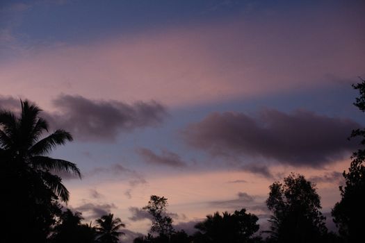 A stunning sunset with dramatic clouds and silhouetted palm trees, creating a moody atmosphere.