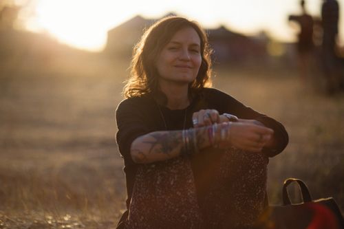 Free A serene image of a tattooed woman sitting on the ground, backlit by a golden hour sunset. Stock Photo