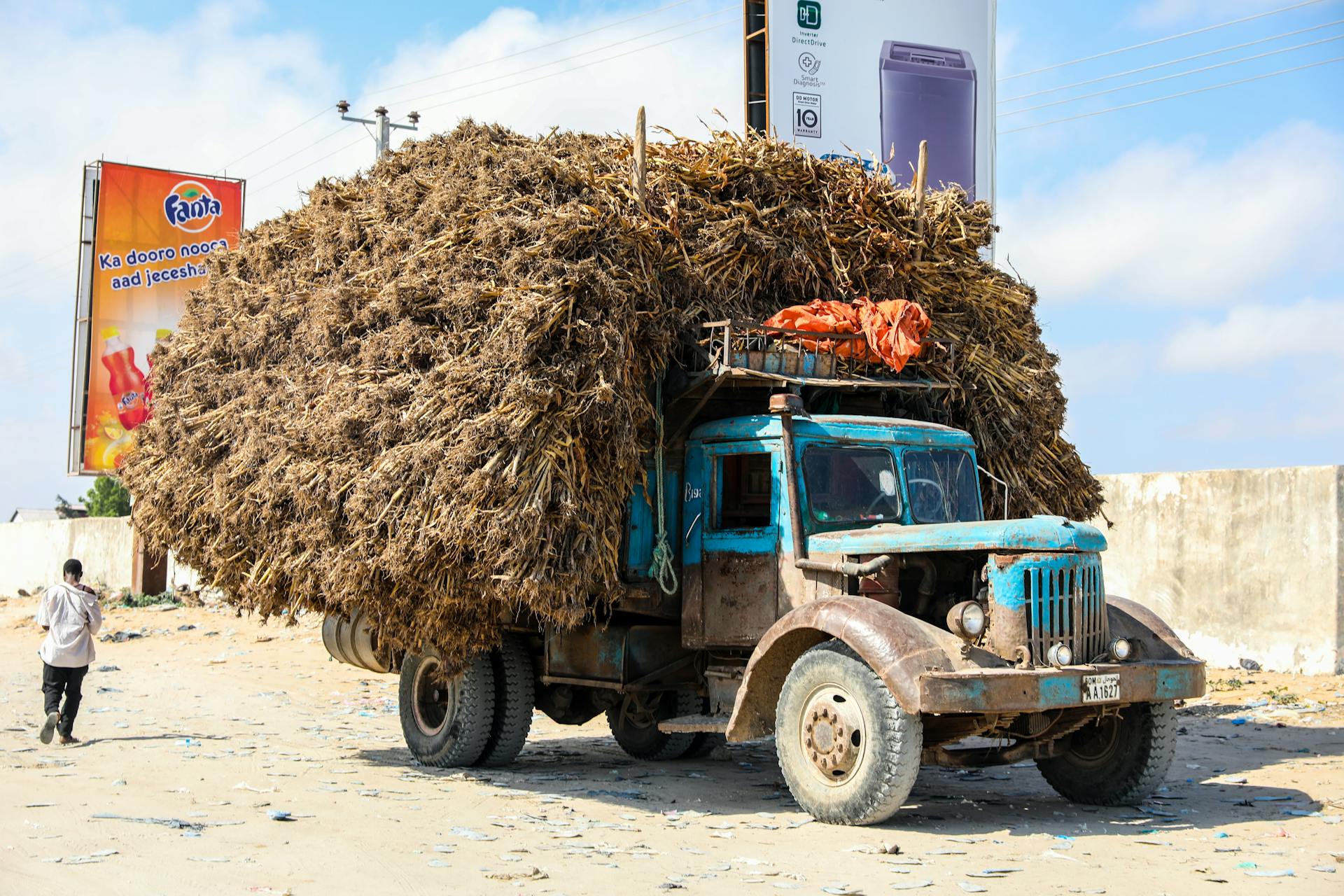 A heavily loaded truck with dried vegetation drives through Mogadishu, Somalia, under sunny skies.