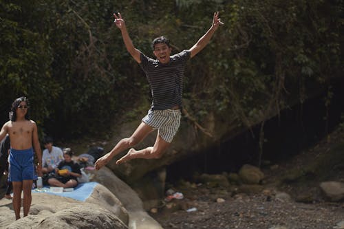 Free Man in Striped Shirt Jumping from a Rock Stock Photo