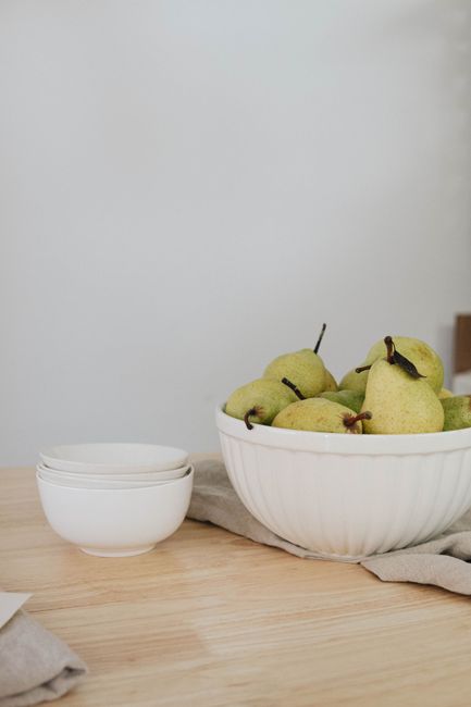 Elegant white bowl filled with fresh pears on a minimalist wooden table setting.