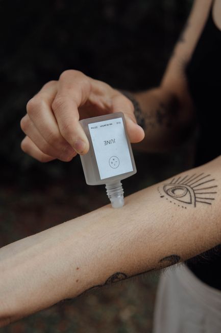 A person with tattoos applies skincare serum on their arm outdoors.