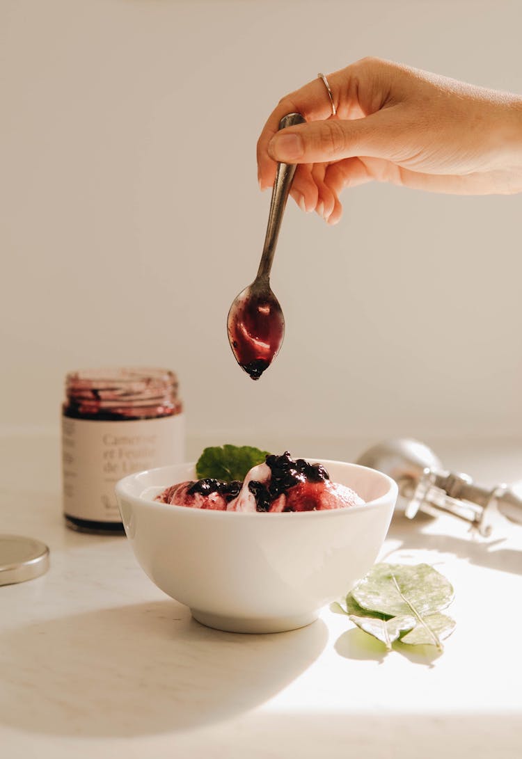 Hand Holding Teaspoon Over Ice Cream In Bowl