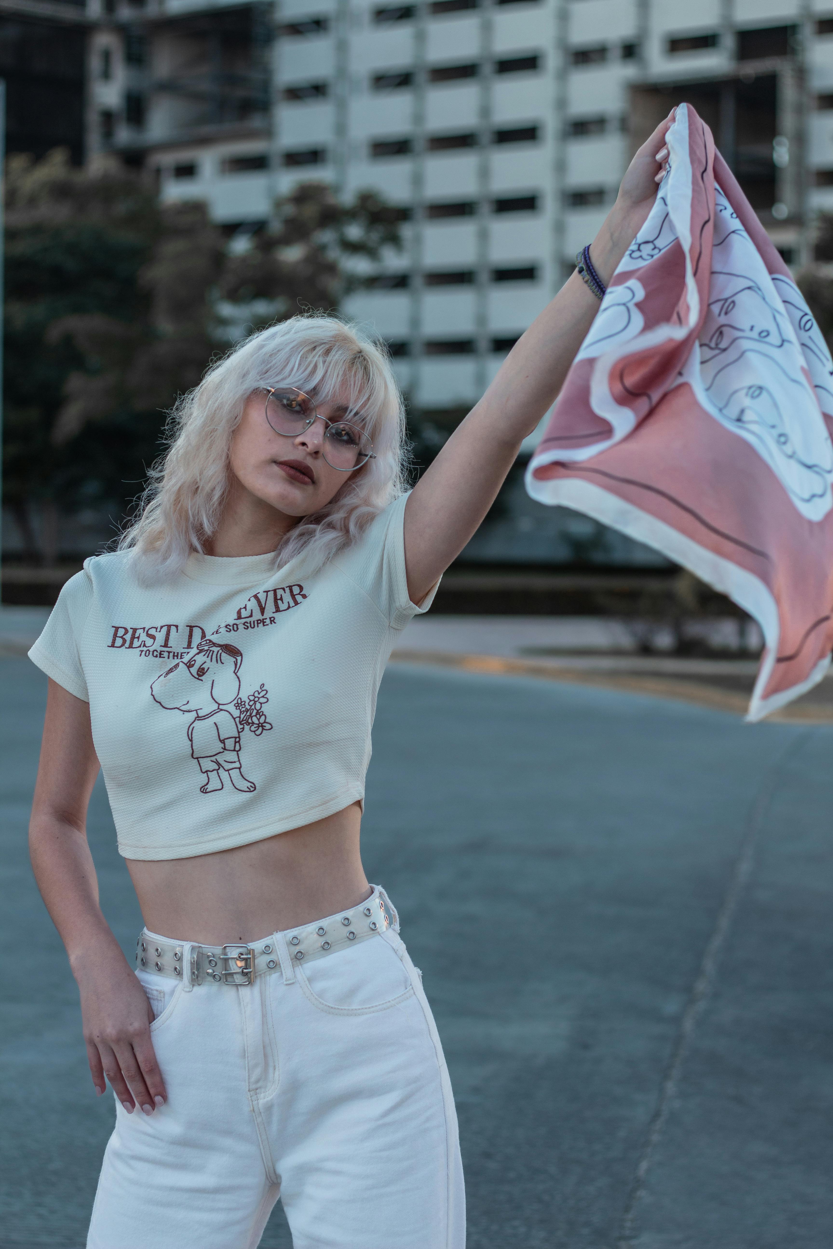 Fashion-forward woman poses outdoors in casual outfit with graphic tee, sunglasses, and vibrant scarf.