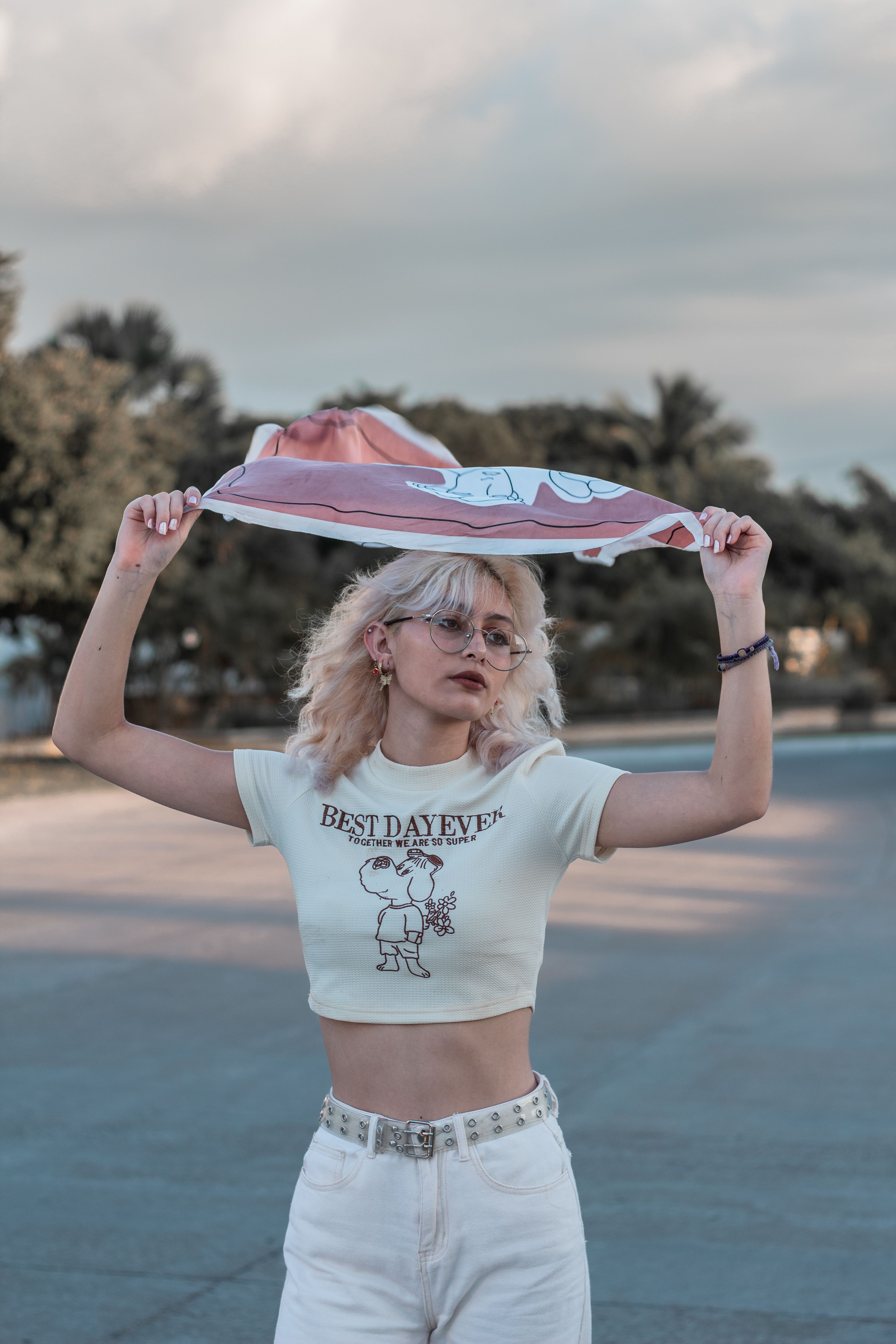 Trendy young woman in a graphic tee holding a pink hat outdoors, radiating casual chic vibes.
