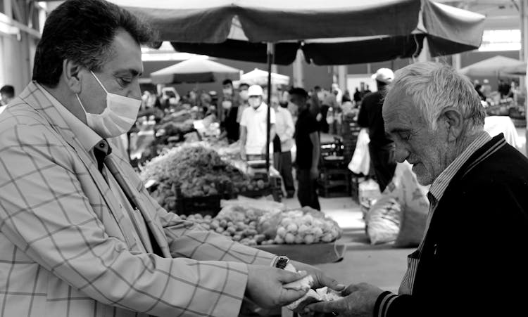 Grayscale Photo Of Man In Stripes Long Sleeve Coat Jacket Sharing Food With An Elderly Man