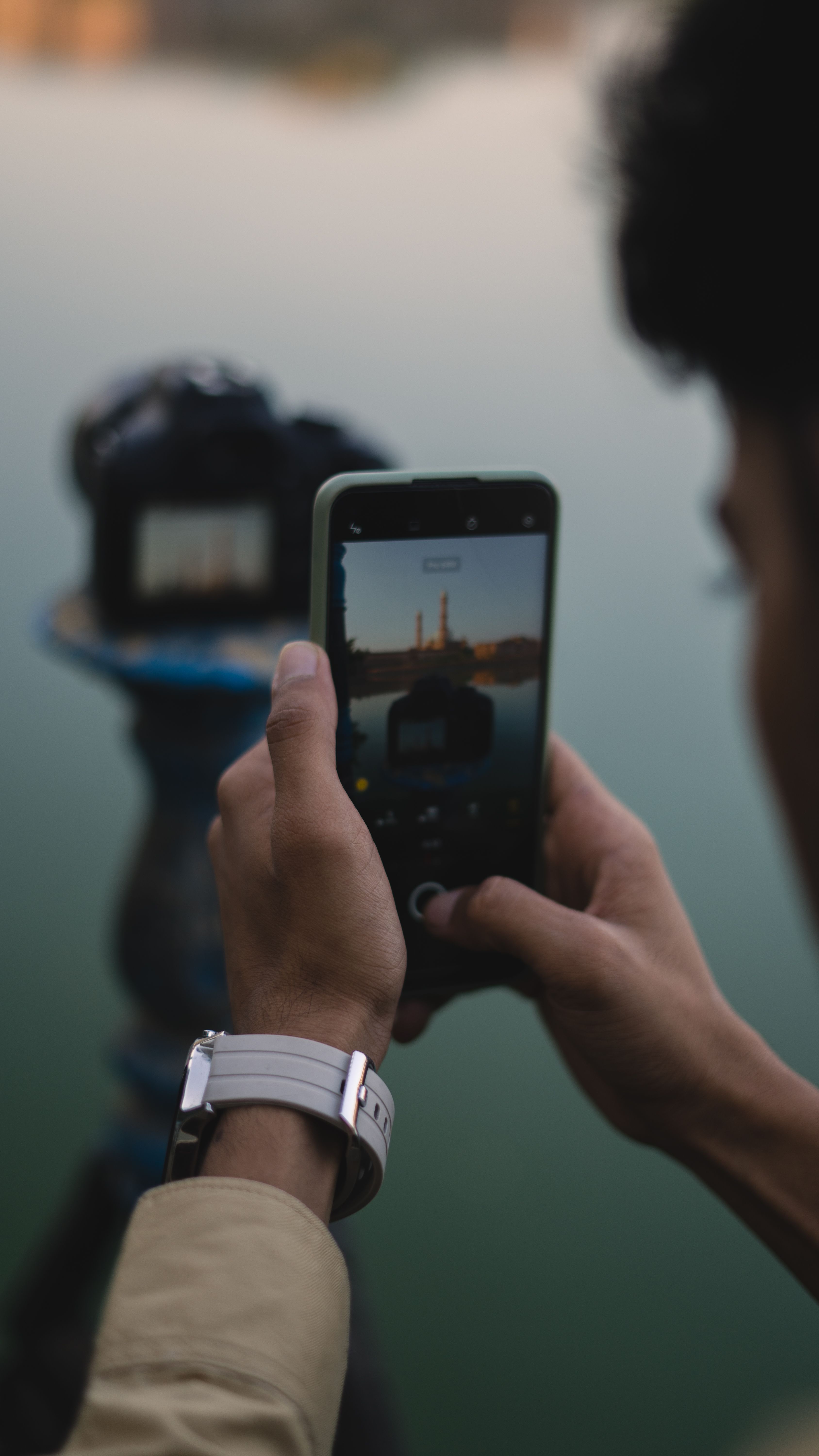 A man captures Bhopal's serene landscape using his smartphone, at twilight.
