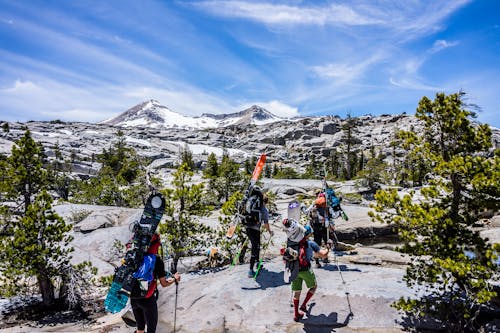 Group of People Hiking With Snowboards Under Blue Cloudy Sky