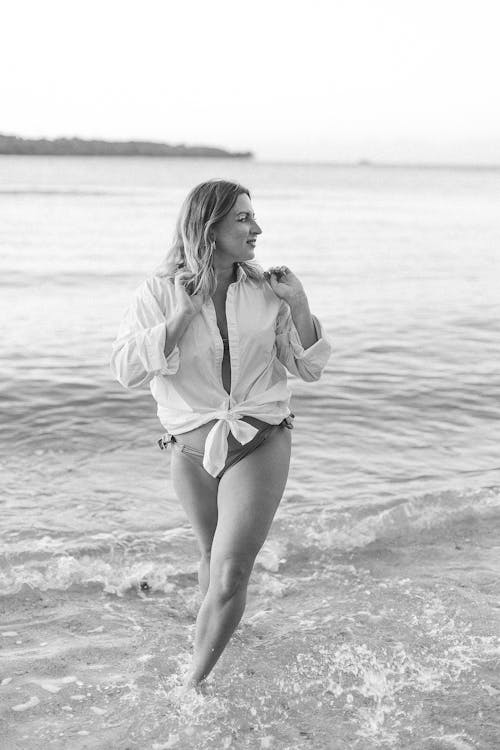 Free Woman Wearing Bikini Under the White Polo Long Sleeves Standing on the Beach while Looking Afar Stock Photo