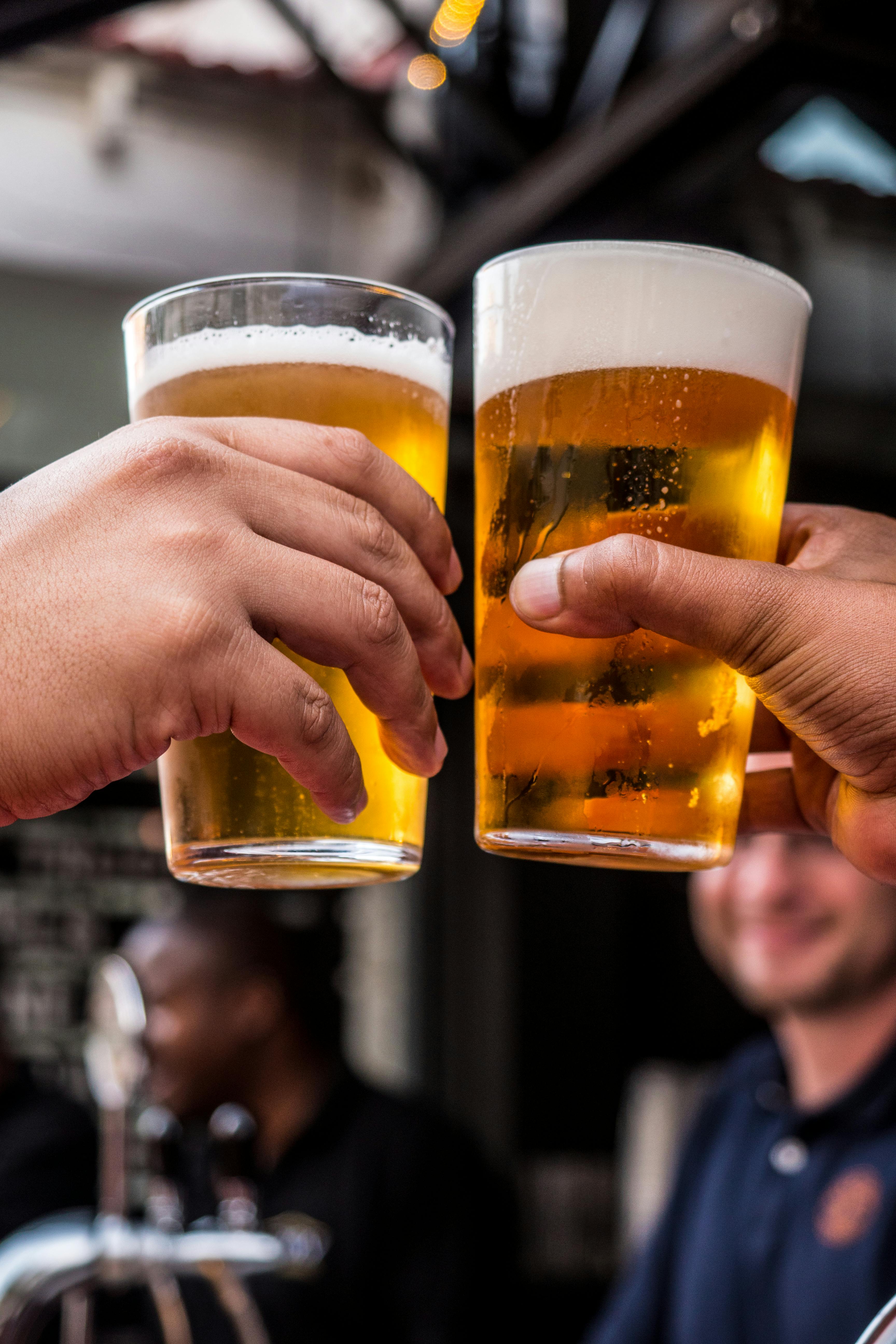 Two persons holding drinking glasses filled with beer. | Photo: Pexels