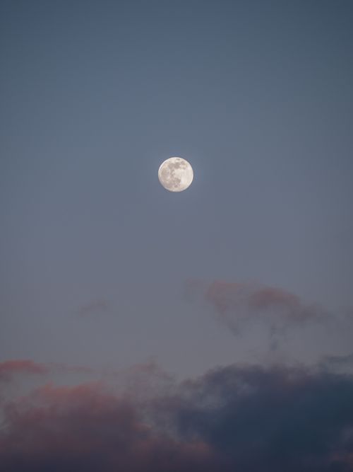 Free A serene full moon set against a gray evening sky with dark clouds. Stock Photo