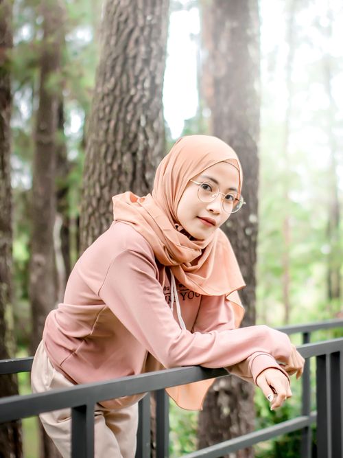 Free A young woman in a hijab and eyeglasses poses confidently by a metal railing in an outdoor setting. Stock Photo