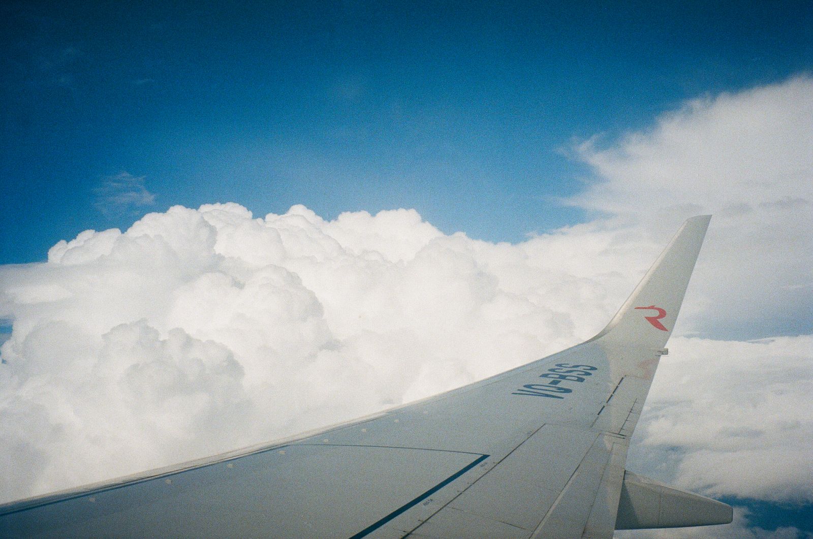View from an aircraft window of a wing above a bright cloudscape.