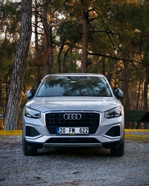 Free A luxury car parked in a forest with autumn foliage creating a serene backdrop. Stock Photo
