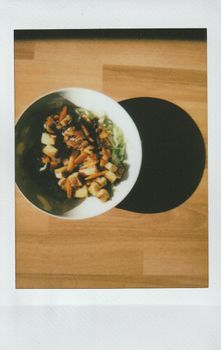 Polaroid instant capture of a tofu and vegetable vegan dish on a wooden table.