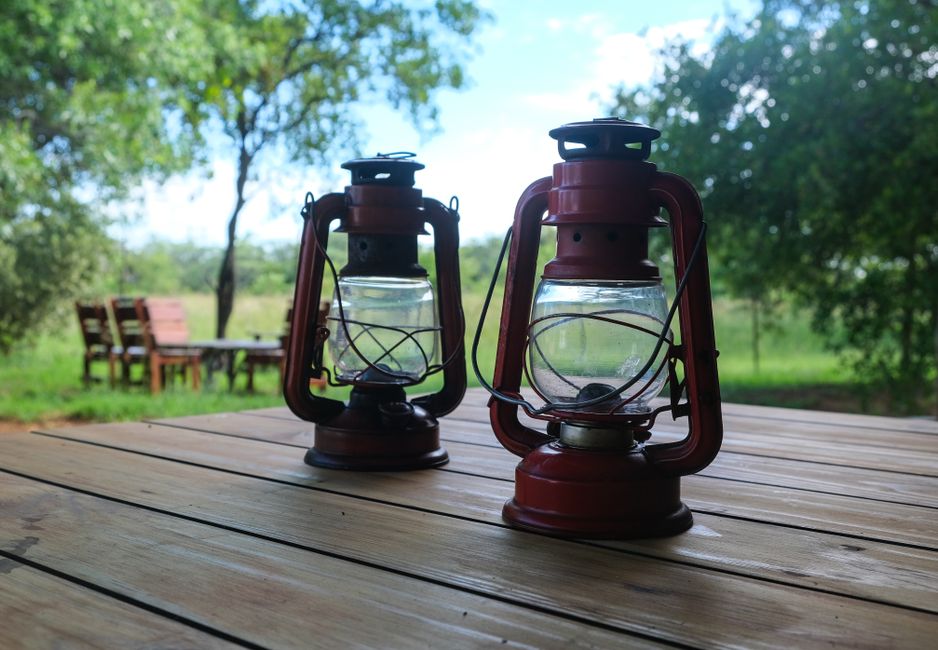 Two vintage gas lamps sit on a wooden table with a lush green background.