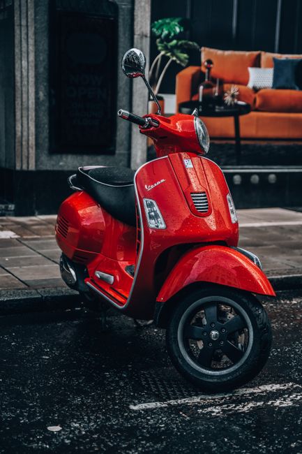A vibrant red Vespa scooter parked on a wet London street, showcasing urban lifestyle.