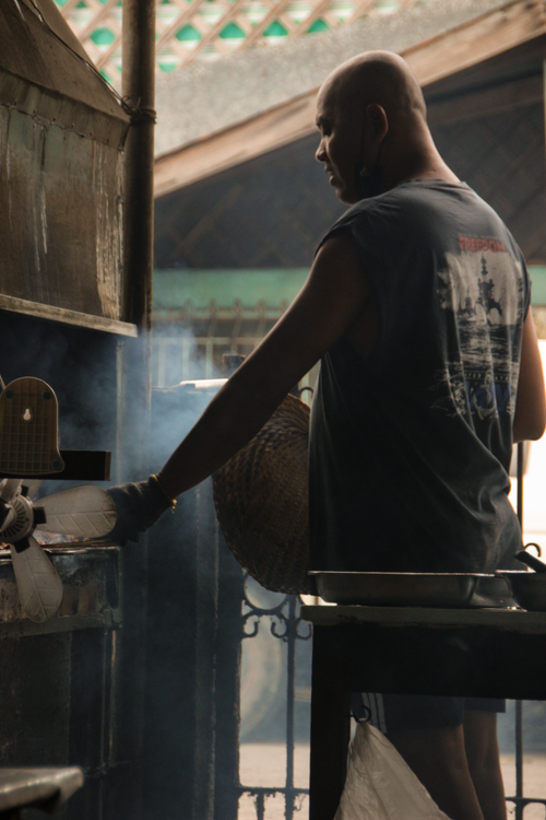 Free Man cooking street food amidst steam in an urban setting, highlighting traditional culinary techniques. Stock Photo