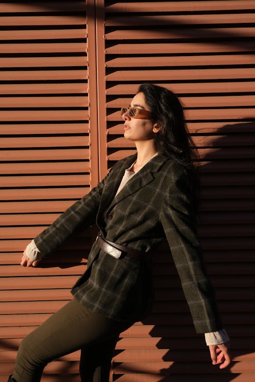A Woman in Black and Gray Plaid Jacket Standing Beside Brown Wall