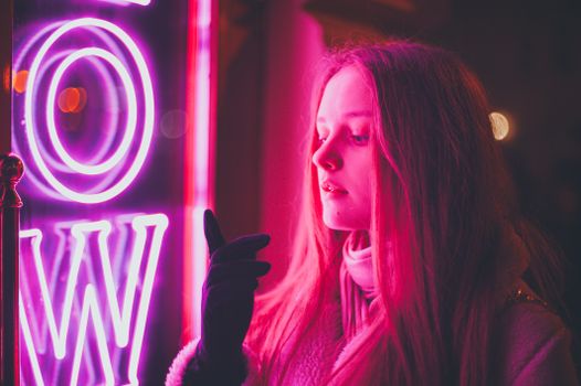 Artistic portrait of a young woman illuminated by vibrant neon lights at night.