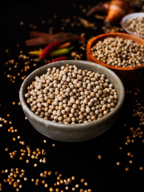 A small bowl of pale ground white pepper next to a pile of whole white peppercorns on a wooden board