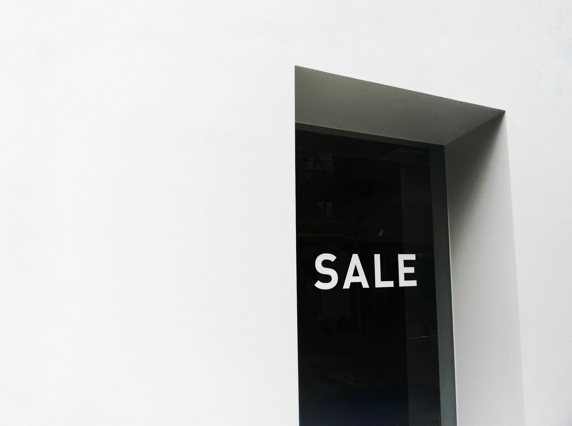 A minimalist black and white image of a sale sign on a store window with ample negative space.