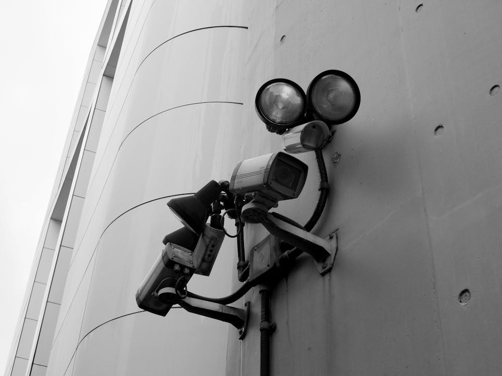 Free Close-up of a black and white CCTV surveillance camera with spotlights mounted on a building wall. Stock Photo