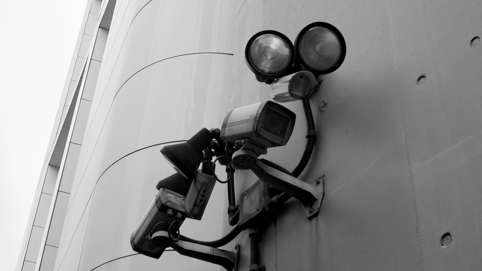 Close-up of a black and white CCTV surveillance camera with spotlights mounted on a building wall.