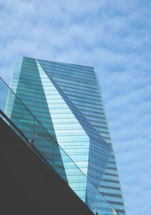 Free A futuristic glass skyscraper towering into a cloud-dappled sky. Stock Photo