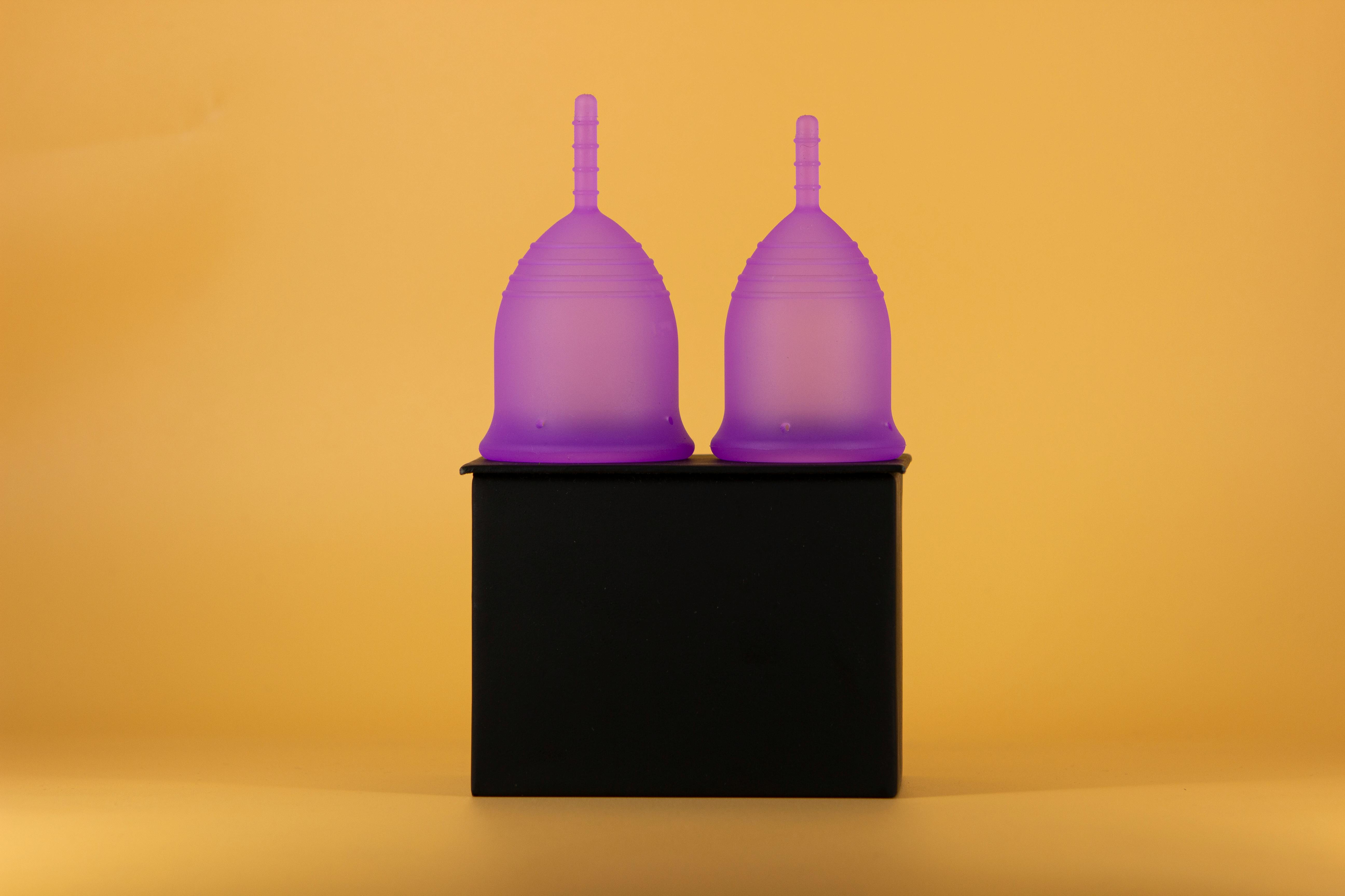Two violet menstrual cups against a vibrant yellow background, emphasizing feminine hygiene products.