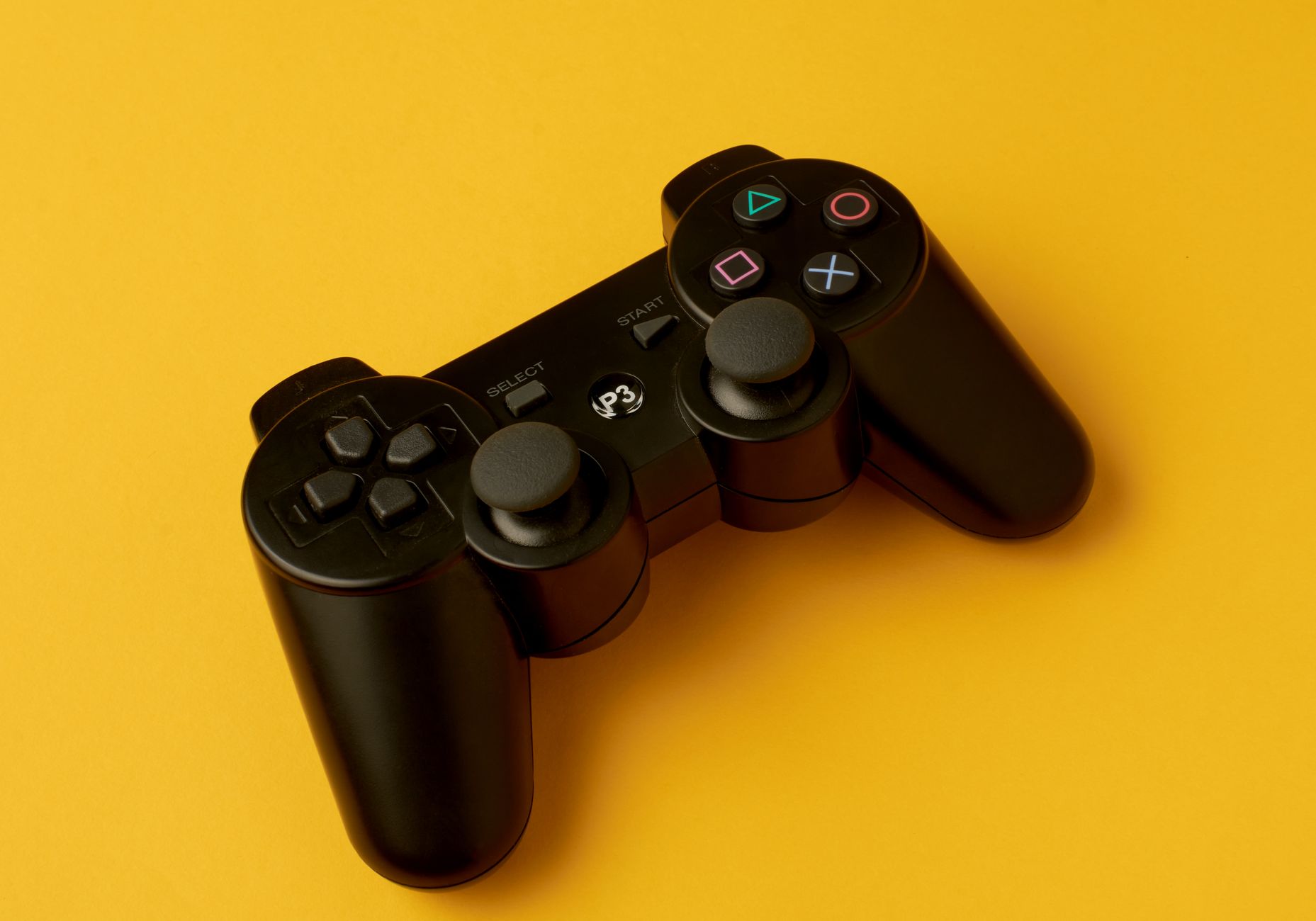 Close-up of a black wireless game controller on a yellow background, emphasizing gaming and electronic aesthetics.