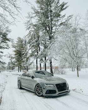 A sleek Audi car parked on a snow-covered road surrounded by winter trees.