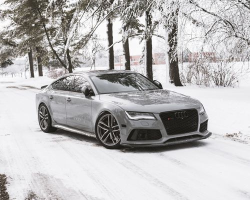 Free A sleek luxury car parked on a snowy road surrounded by trees in a winter landscape. Stock Photo