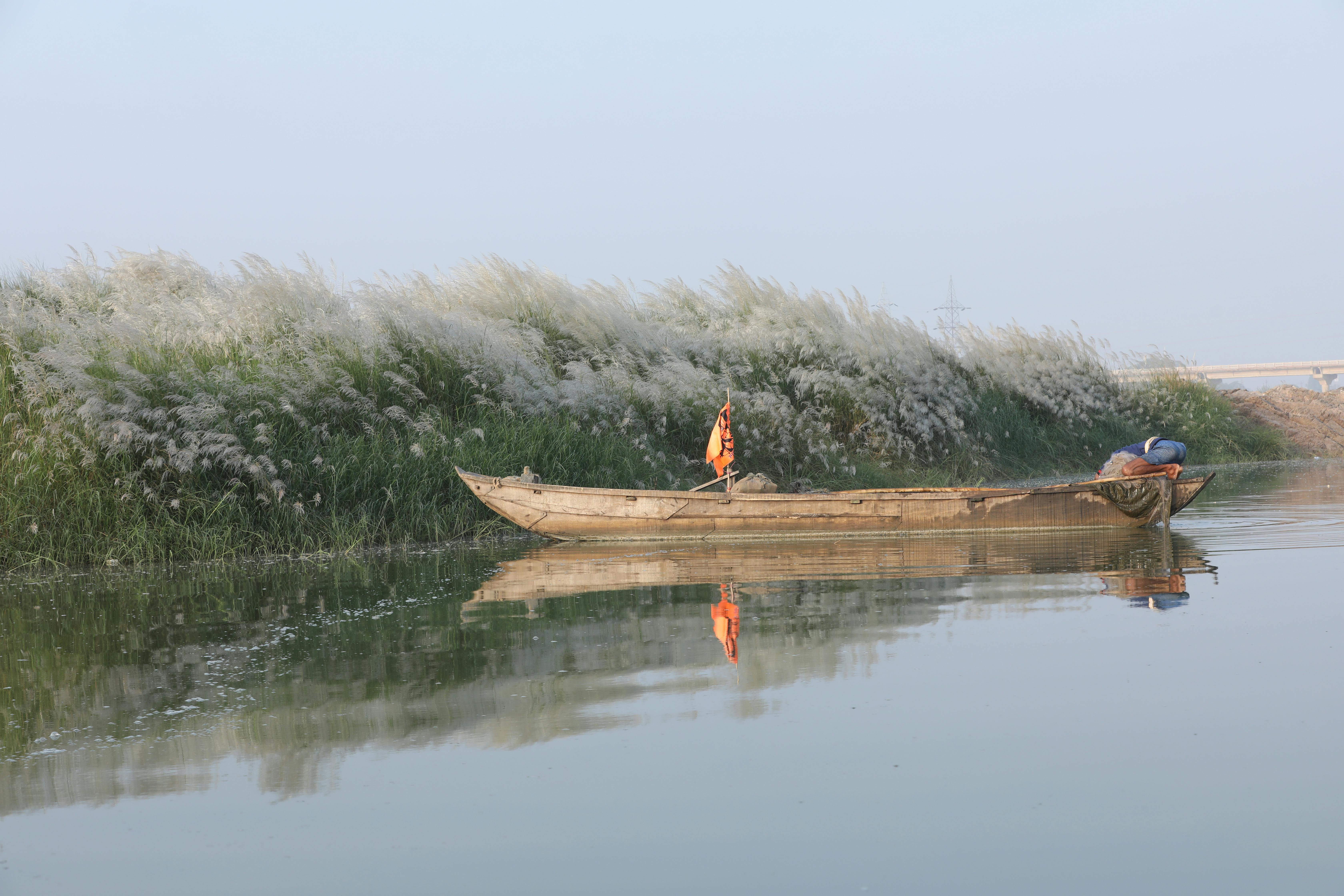 Peaceful river landscape with a reflection of a wooden boat and lush grass on a calm morning.