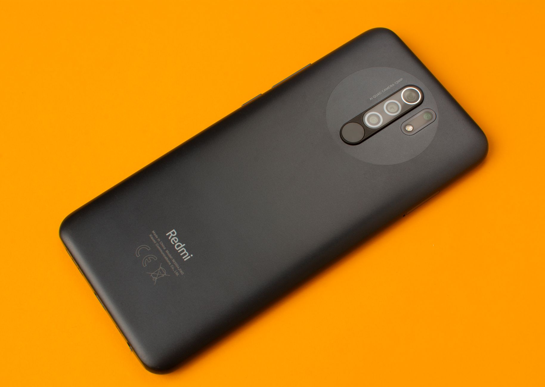 Black smartphone placed on a vivid orange background, showcasing sleek design and multiple cameras.
