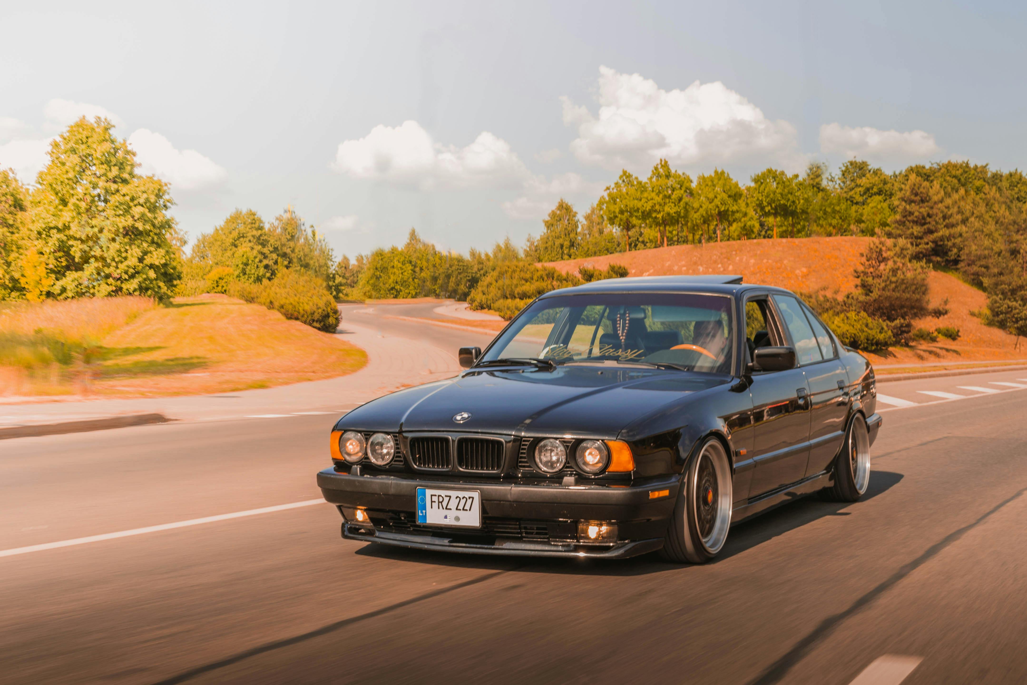A stylish black BMW cruising along a winding scenic road under a clear sky.