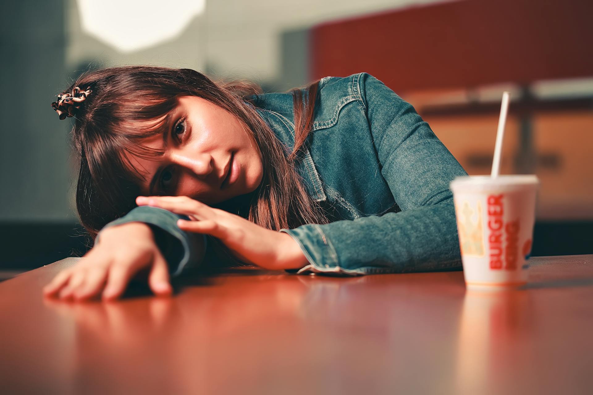 Casual portrait of a young woman in a denim jacket at a fast food restaurant, leaning on a table.