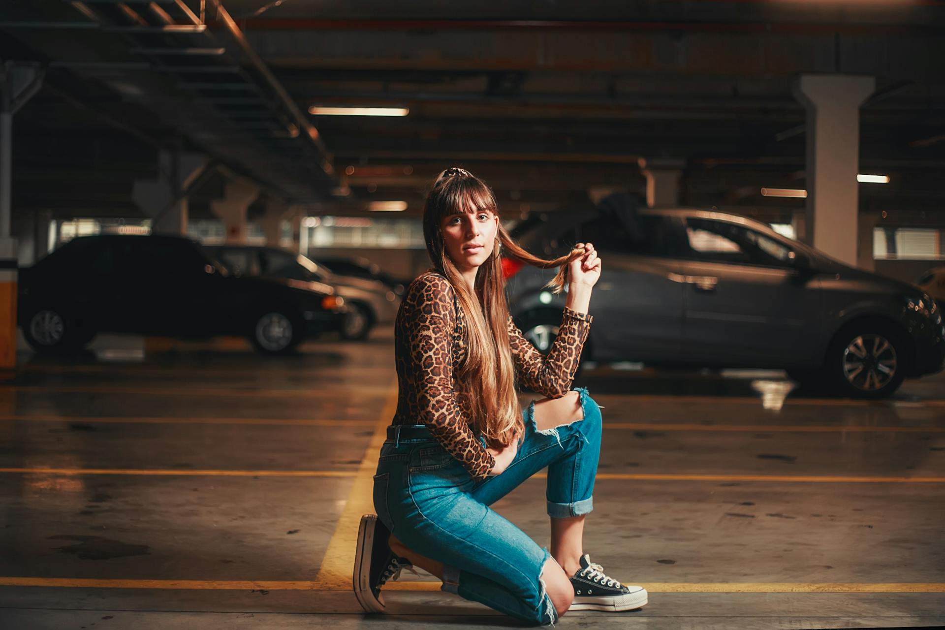 Stylish woman in leopard print shirt squatting in a parking garage, creating a modern urban vibe.