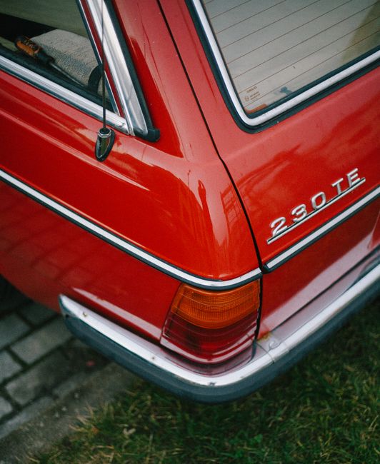 Close-up of vintage red 230 TE car parked outdoors with grass and pavement, perfect for classic car enthusiasts.
