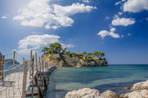 Brown Wooden Bridge over Blue Sea Under Blue and White Cloudy Sky