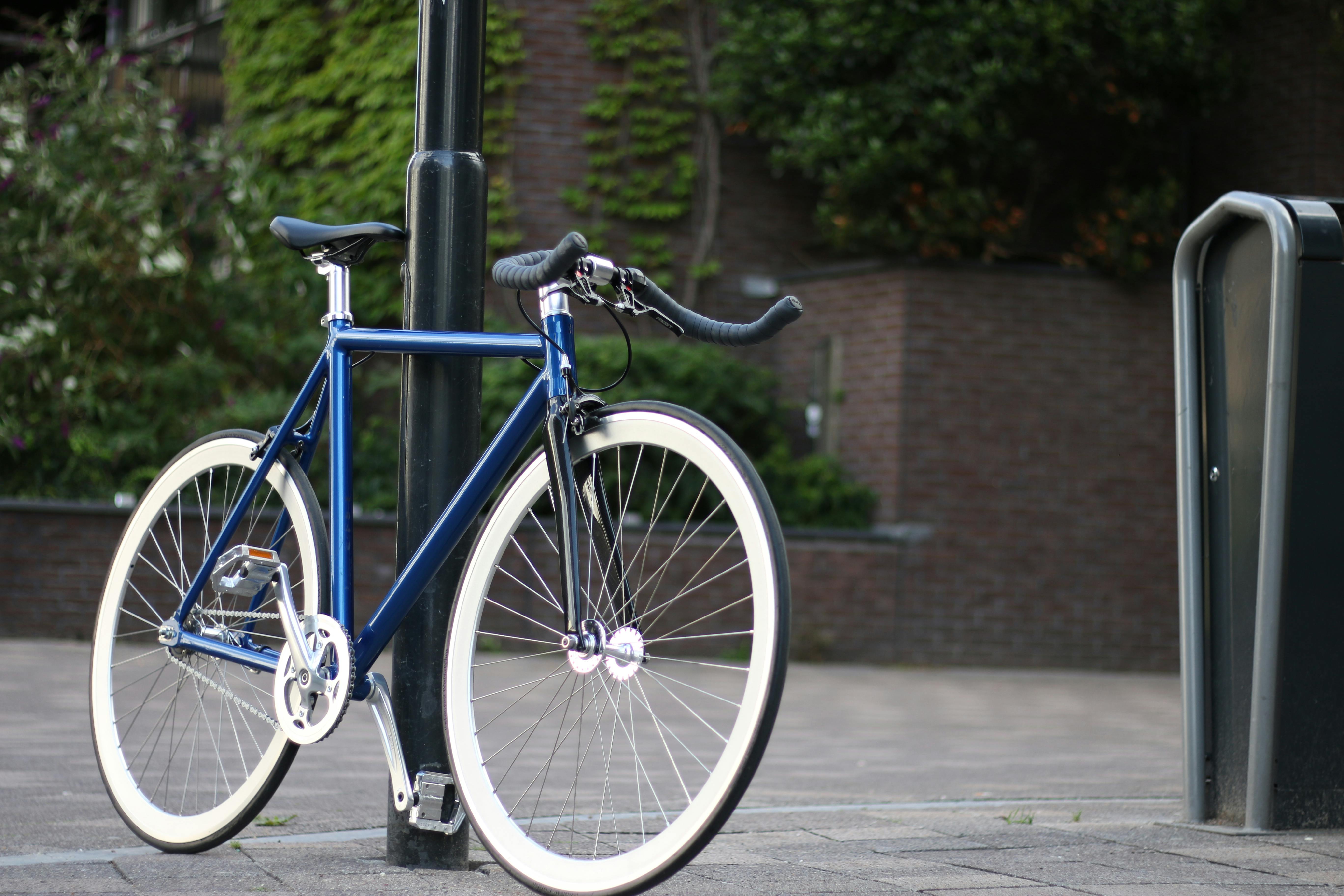 Free Urban scene with a blue bicycle resting against a streetlight on a city sidewalk. Stock Photo