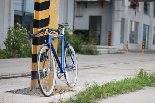 A blue bicycle parked against a yellow and black striped pole in an urban setting.
