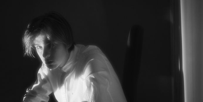 Dramatic light and shadow create a moody portrait of a young man in monochrome.