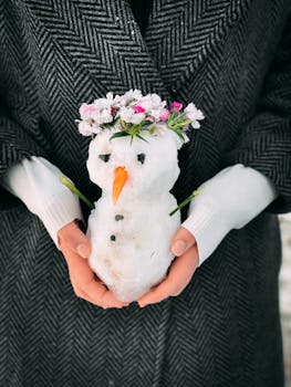 A small snowman with a flower crown held by a person in winter attire.