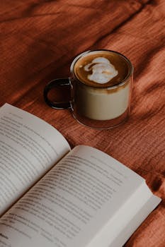 Aesthetic setup of a coffee cup and open book on a warm brown blanket.